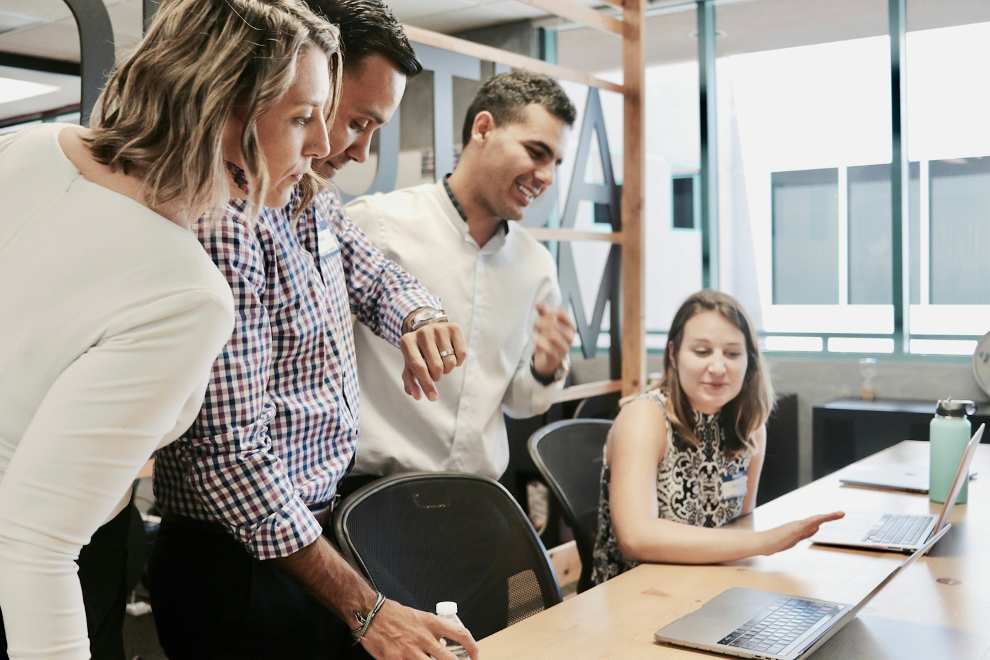 Professionisti diversi collaborano al computer portatile a un tavolo di legno chiaro.